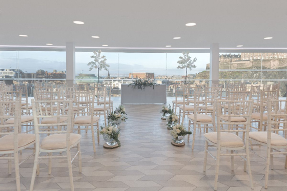 Ceremony set up in the SKYBar with views across Edinburgh, featuring white chiavari chairs and other white decor